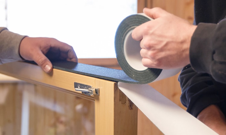 Hands applying painter's tape to cabinet edge